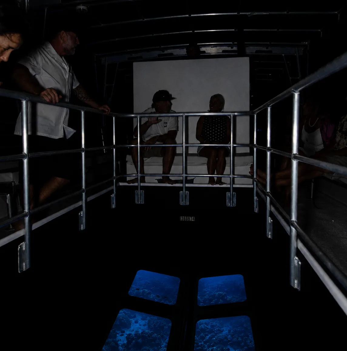 Guests stand at the rail around the viewing well in low light, with the glass panes glowing blue.